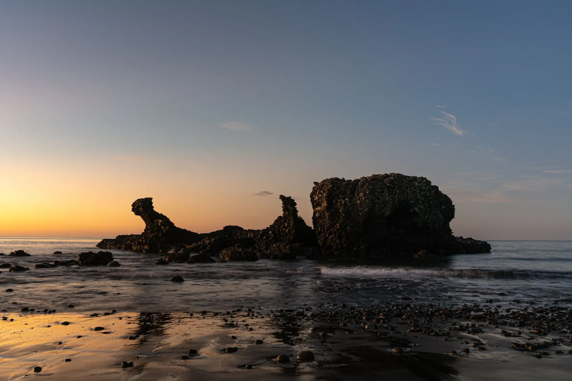 The rock formation at El Tunco beach silhouetted at sunset over wet volcanic sand.
