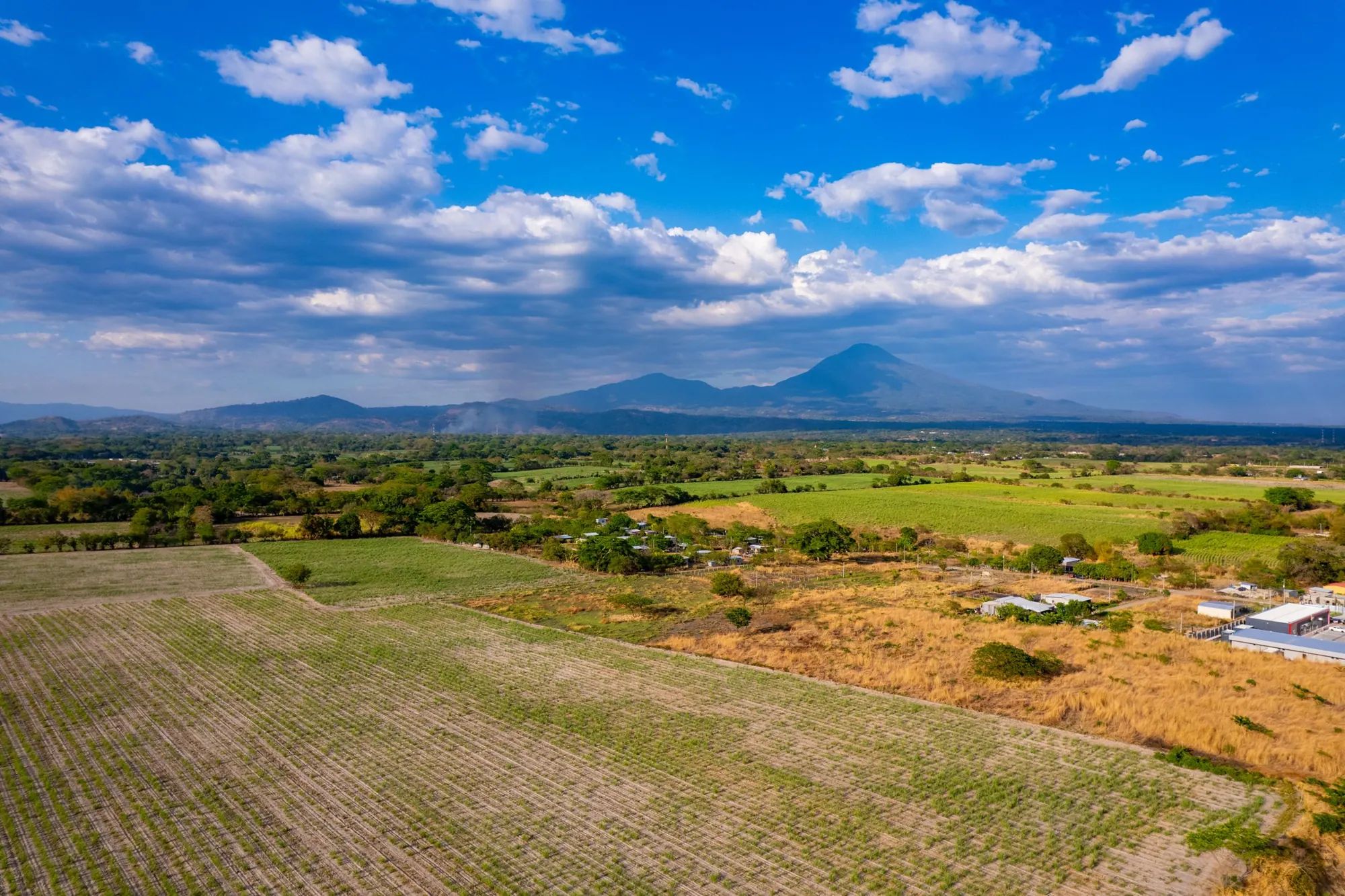 Plowed fields and pasture in the Salvadoran countryside with a volcano in the distance.