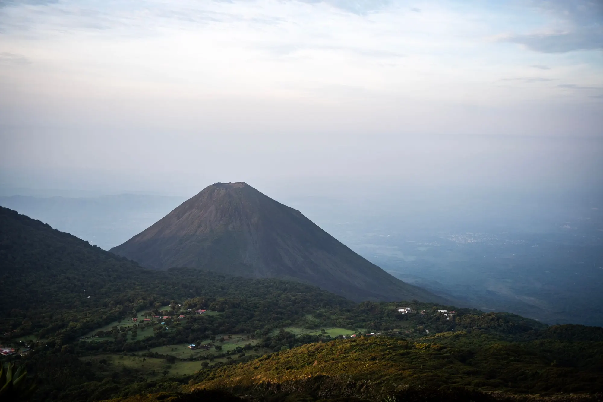 Izalco volcano rising over misty farmland at dawn.