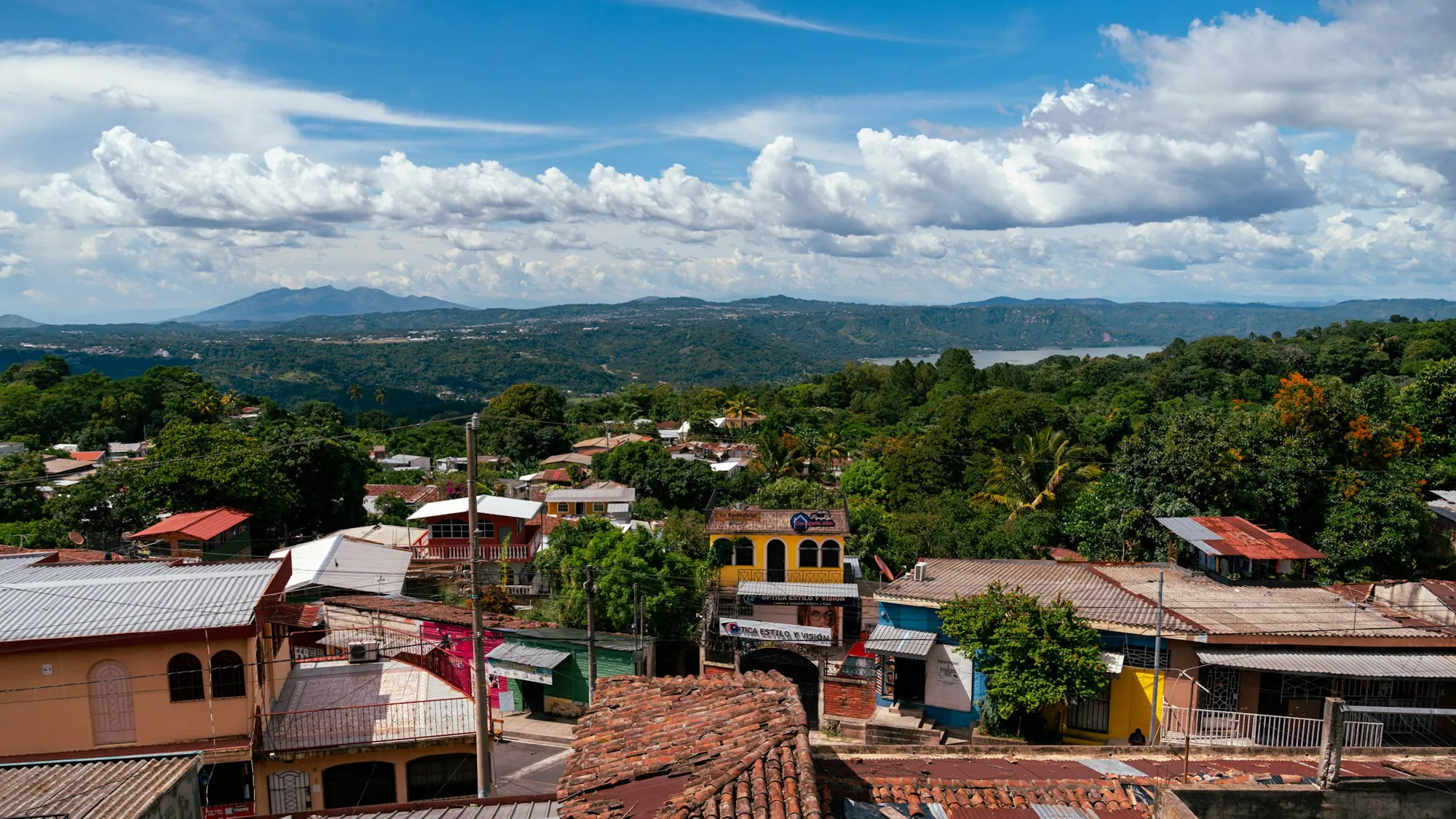Tile and metal rooftops of Santiago Texacuangos with green hills and Lake Ilopango behind.